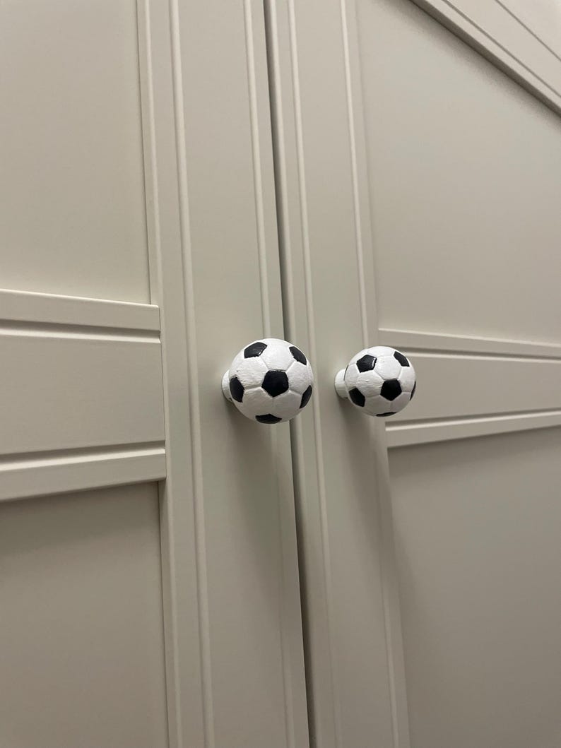 May include: Two white soccer ball shaped cabinet knobs with black stitching.
