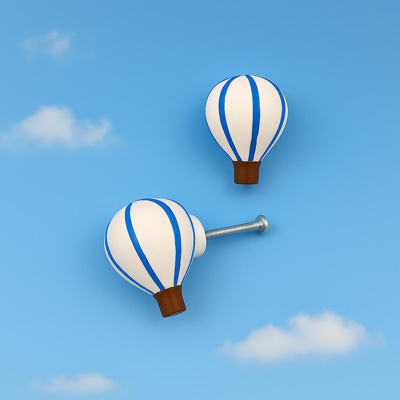May include: Two hot air balloon-shaped cabinet knobs. The knobs are white with blue stripes and brown bases. One knob has a silver screw attached. The background is a light blue sky with white clouds.