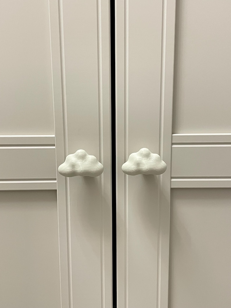 Op de afbeelding: Witte kastdeuren met wolkvormige handgrepen. De kastdeuren zijn wit geschilderd en hebben een eenvoudig, modern design. De wolkvormige handgrepen geven de kast een speelse uitstraling.