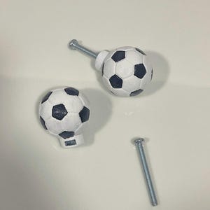 May include: Two white soccer ball shaped cabinet knobs with black stitching and a silver screw.