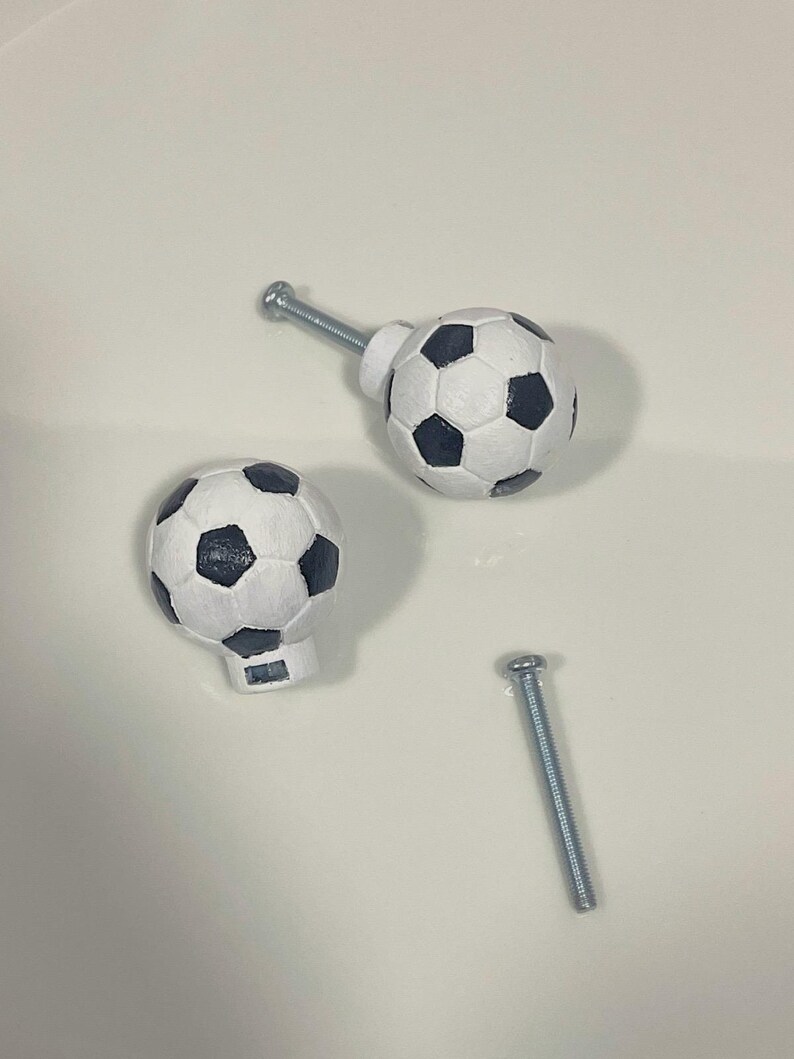 May include: Two white soccer ball shaped cabinet knobs with black stitching and a silver screw.