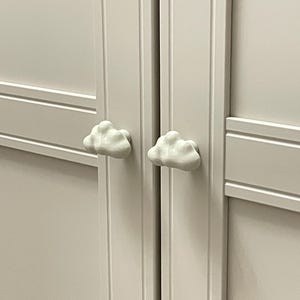 Op de afbeelding: Detail van een witte kastdeur met twee wolkvormige handgrepen. De witte wolkenknoppen geven de kastdeur een speelse uitstraling.