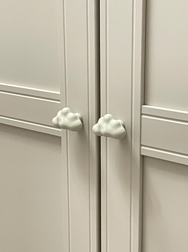 Op de afbeelding: Detail van een witte kastdeur met twee wolkvormige handgrepen. De witte wolkenknoppen geven de kastdeur een speelse uitstraling.