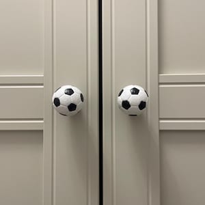 Puede incluir: Dos puertas de armario blancas con pomos de puerta en forma de balón de fútbol negro.