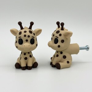 Peut inclure: Deux boutons de meuble en forme de girafe. Les boutons sont de couleur beige clair avec des taches et des accents brun fonc&eacute;. Chaque girafe a une vis m&eacute;tallique pour l'installation. Les girafes sont assises avec de grands yeux noirs.
