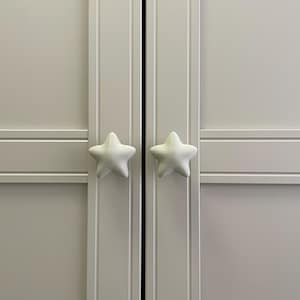 May include: A close-up of a light gray cabinet with two doors. Each door has a white, star-shaped knob. The knobs are textured and add a whimsical touch to the otherwise simple design. The cabinet is likely for storage.