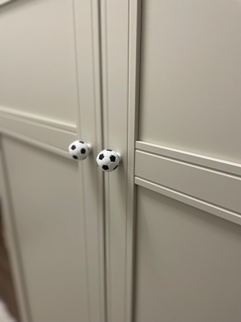May include: Two white cabinet doors with black soccer ball-shaped knobs.