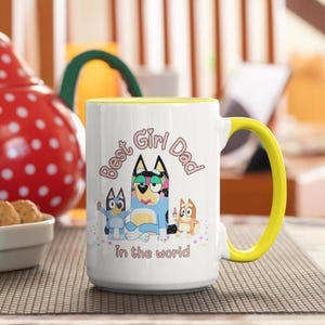 Może przedstawiać: Biały kubek ceramiczny z ż&oacute;łtym rantem i uchwytem. Kubek przedstawia kresk&oacute;wkową grafikę trzech ps&oacute;w z tekstem "Best Girl Dad in the world".