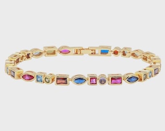 May include: Gold-toned bracelet featuring a series of colorful gemstones in various shapes. The gemstones include red, blue, pink, and green stones. The bracelet has a clasp closure.