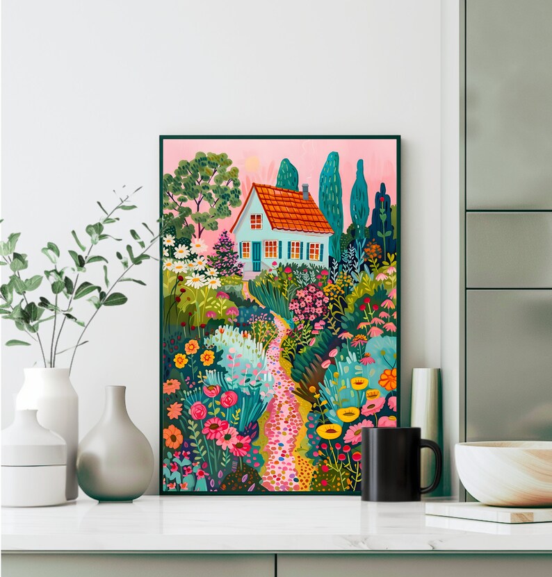 May include: A framed art print showing a garden path leading to a light blue house with an orange roof. The artwork features vibrant flowers, trees, and a pink sky, creating a whimsical scene. The print is displayed on a white surface.