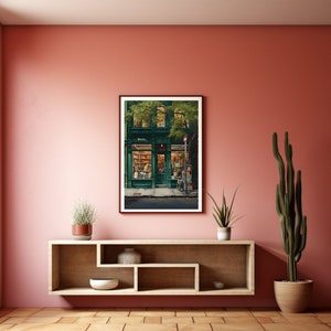 May include: A framed print depicting a green-fronted bookstore with the word "Books" above the door. The interior is illuminated, revealing bookshelves. The print is displayed on a pink wall above a wooden shelf with plants and ornaments.