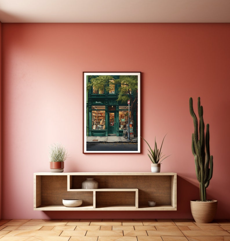 May include: A framed print depicting a green-fronted bookstore with the word "Books" above the door. The interior is illuminated, revealing bookshelves. The print is displayed on a pink wall above a wooden shelf with plants and ornaments.