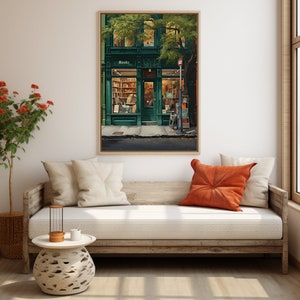 May include: A framed print of a charming bookstore with a green exterior and the word "Books" above the door. The interior is illuminated, revealing bookshelves. The artwork hangs on a neutral wall, with a wooden sofa and cushions in the foreground.