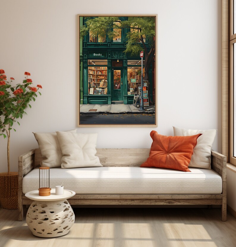 May include: A framed print of a charming bookstore with a green exterior and the word "Books" above the door. The interior is illuminated, revealing bookshelves. The artwork hangs on a neutral wall, with a wooden sofa and cushions in the foreground.