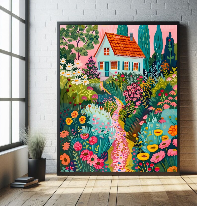 May include: A framed art print showing a vibrant garden scene with a light blue house, an orange roof, and a winding path. The garden is filled with flowers in shades of pink, yellow, and white, set against a pink sky. The artwork is framed in black.