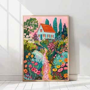 May include: A framed art print showing a garden scene. A small house with a red tiled roof and blue shutters is surrounded by colourful flowers and greenery. A stone path winds through the garden, set against a pink sky. The artwork is in a wooden frame.