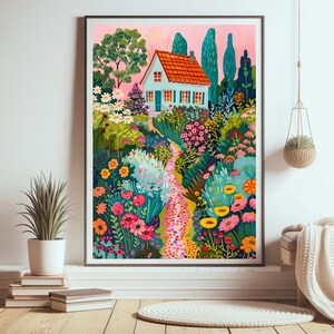 May include: A framed art print showing a vibrant garden scene with a light blue house, orange roof, and a winding path. The garden is filled with flowers in pink, yellow, and green. The artwork is displayed on a white wall.