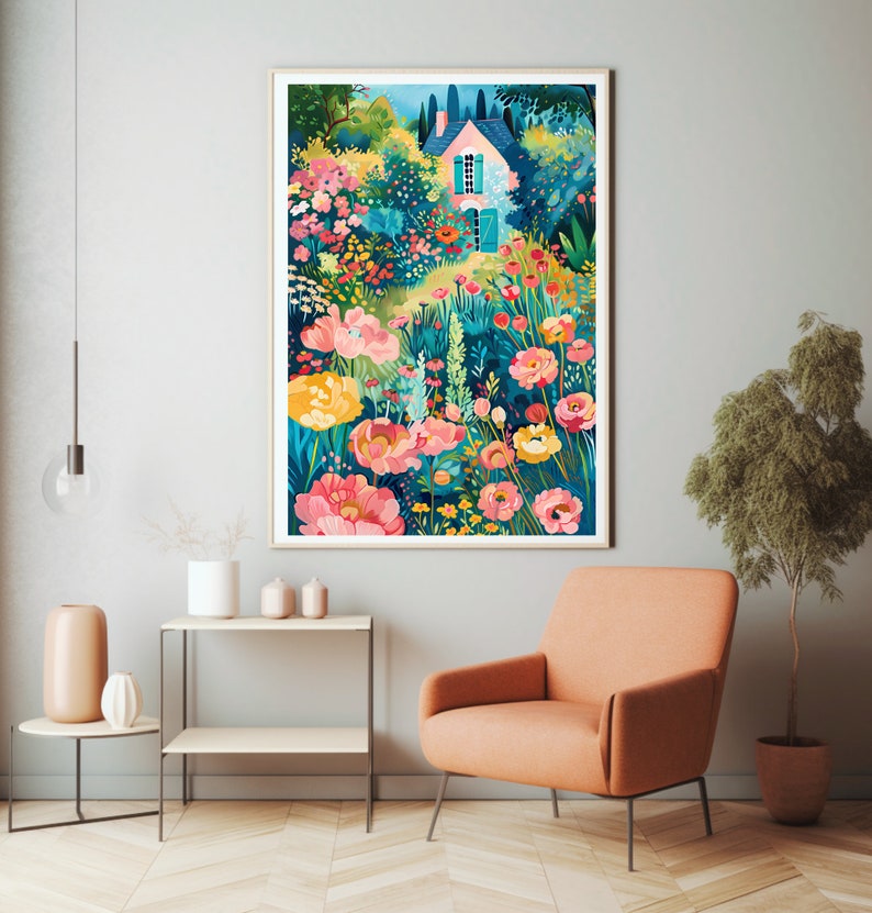 May include: A framed art print depicts a colorful garden scene with a pink house. The artwork features vibrant pink, yellow, and red flowers, lush greenery, and a blue sky. The print is displayed in a living room setting with an orange armchair and side table.