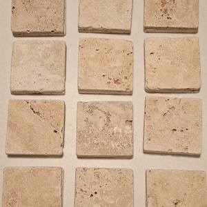 Könnte beinhalten: Zwölf quadratische beige Travertin-Fliesen mit einer rauen, strukturierten Oberfläche.