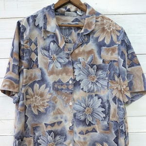 May include: A blue and brown short-sleeved button-up shirt with a floral print. The shirt has a collared neckline and a single chest pocket.
