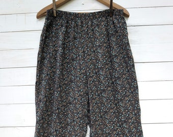 May include: Black pants with a floral print featuring small blue and brown flowers. The pants have a wide leg and an elastic waistband.