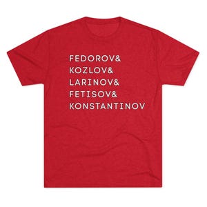 May include: A red t-shirt with white text. The text includes the names FEDOROV, KOZLOV, LARINOV, FETISOV, and KONSTANTINOV. The shirt is made of a soft material.