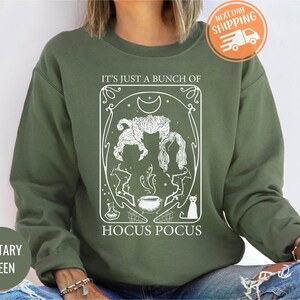 May include: A green sweatshirt with a white graphic design featuring a witch's cauldron, a cat, and the text "It's just a bunch of Hocus Pocus".