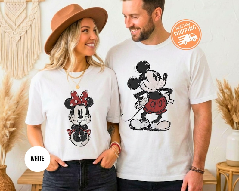 May include: White t-shirts featuring Mickey and Minnie Mouse designs. The Minnie Mouse shirt has a red polka dot bow. The Mickey Mouse shirt has a red skirt. The shirts are worn by a couple.