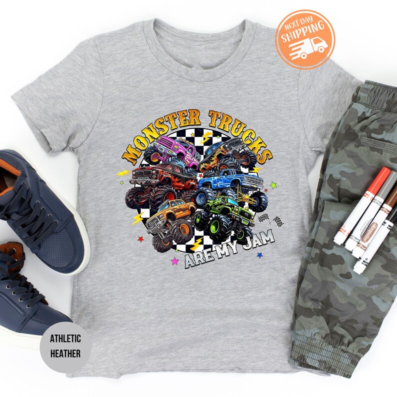 Puede incluir: Una camiseta gris jaspeado con un gr&aacute;fico colorido de monster trucks. El texto "MONSTER TRUCKS ARE MY JAM" est&aacute; impreso en la camiseta. La imagen tambi&eacute;n incluye zapatillas azules y pantalones de camuflaje.