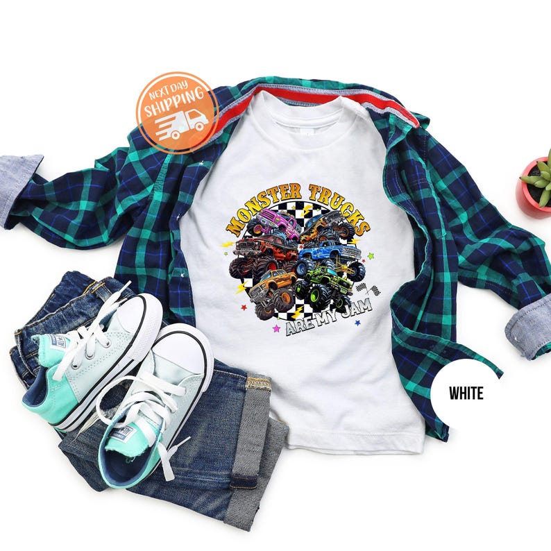 Puede incluir: Camiseta blanca con un gr&aacute;fico colorido de monster trucks y el texto "MONSTER TRUCKS ARE MY JAM". La imagen incluye vaqueros azules, una camisa a cuadros y zapatillas de deporte azul claro.
