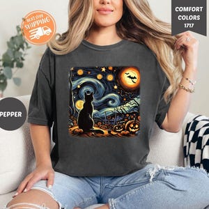 May include: Dark grey t-shirt featuring a Halloween-themed graphic. The design includes a black cat silhouette, pumpkins, and a starry night sky with a full moon. The shirt also has the text "COMFORT COLORS 1717" and "PEPPER".
