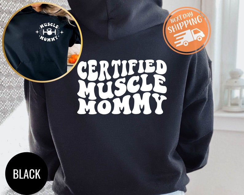 Op de afbeelding: Zwarte hoodie met een witte afbeelding met de tekst "CERTIFIED MUSCLE MOMMY" in een retro-lettertype.