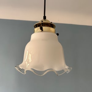 Könnte beinhalten: Eine weiße Glas-Pendelleuchte mit einem gewellten Rand und einer Messing-Oberfläche.