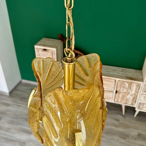 May include: A gold chain hangs from a ceiling, supporting a gold and amber glass pendant light fixture. The fixture is shaped like a flower with multiple petals.