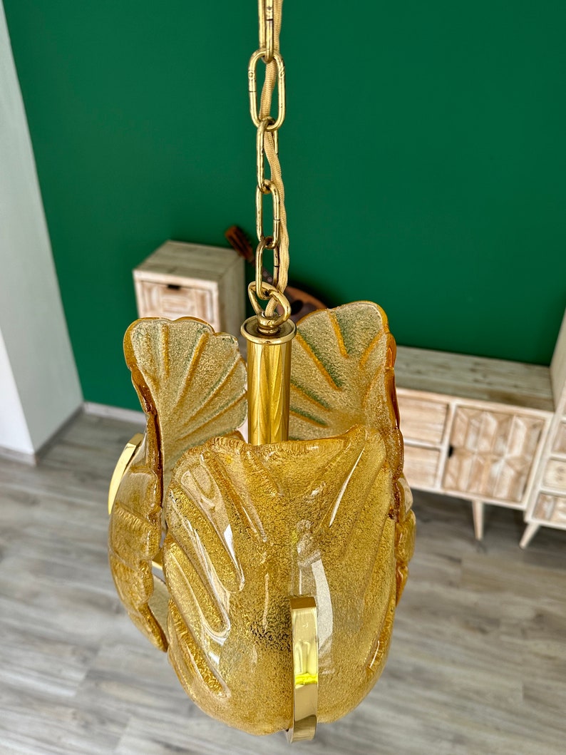 May include: A gold chain hangs from a ceiling, supporting a gold and amber glass pendant light fixture. The fixture is shaped like a flower with multiple petals.
