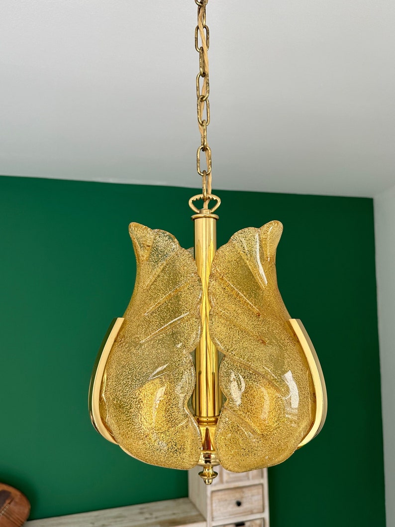 May include: A gold chain hangs from a ceiling, supporting a yellow glass chandelier with a textured surface. The chandelier has a unique, organic shape resembling a flower.