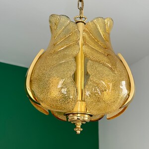May include: A gold-toned pendant light fixture with a frosted glass shade. The shade is shaped like a flower with multiple petals. The light fixture is hanging from a chain.