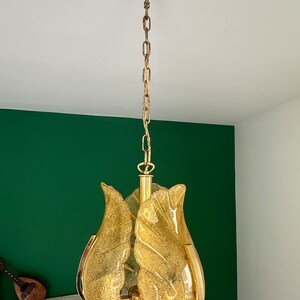 May include: A gold-toned chandelier with a chain hanging from the ceiling. The chandelier has a cluster of four yellow glass shades that resemble flower petals.