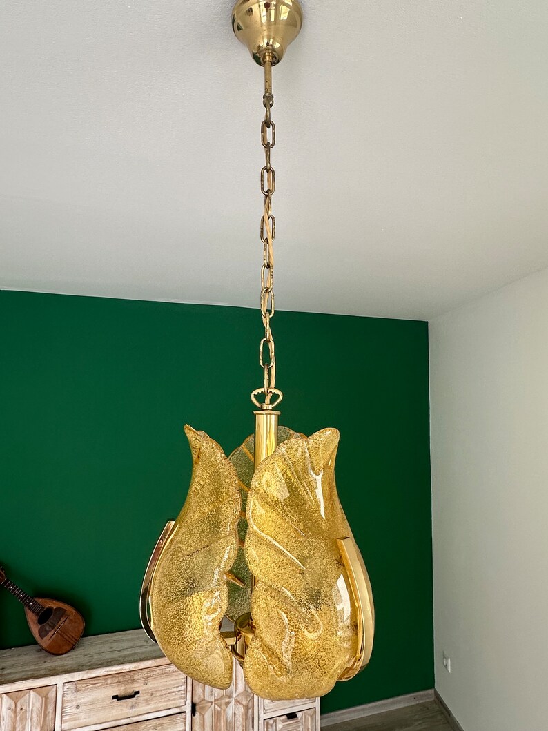 May include: A gold-toned chandelier with a chain hanging from the ceiling. The chandelier has a cluster of four yellow glass shades that resemble flower petals.