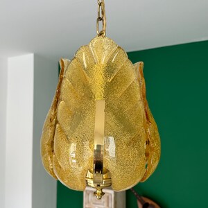 May include: A gold chain hangs from the ceiling, supporting a yellow glass pendant light fixture. The fixture is shaped like a flower with multiple petals.