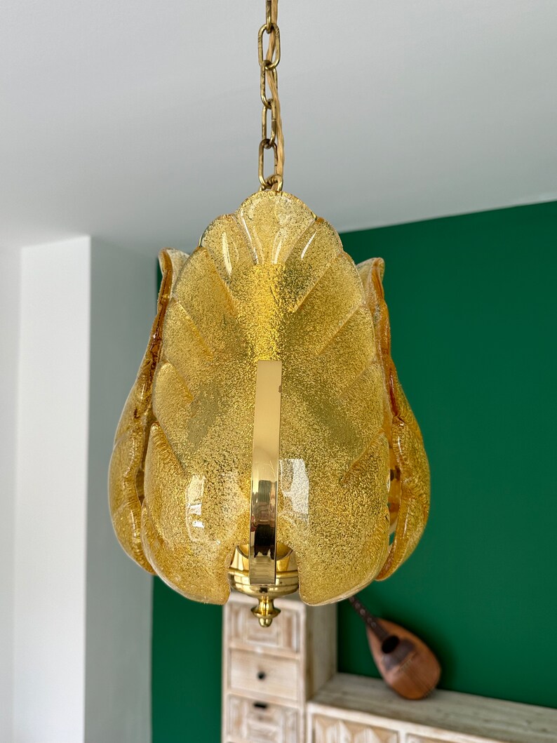 May include: A gold chain hangs from the ceiling, supporting a yellow glass pendant light fixture. The fixture is shaped like a flower with multiple petals.