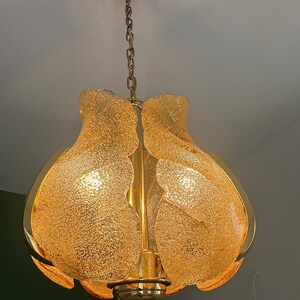 May include: A gold-toned chandelier with a chain hanging from the ceiling. The chandelier has a frosted glass shade with a textured surface.
