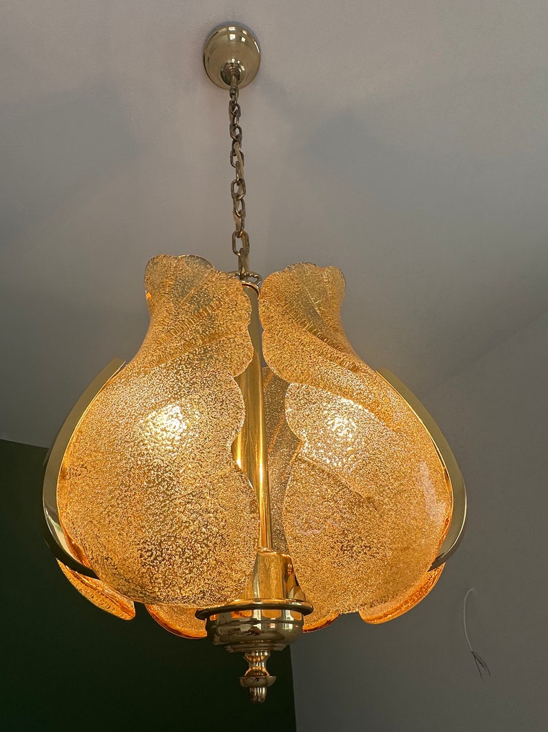 May include: A gold-toned chandelier with a chain hanging from the ceiling. The chandelier has a frosted glass shade with a textured surface.