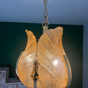 May include: A gold-toned chandelier with a chain and multiple frosted glass shades. The shades are shaped like leaves and have a textured surface.