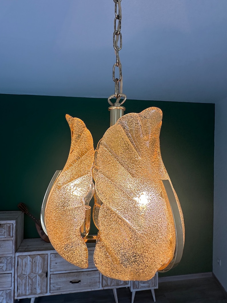 May include: A gold-toned chandelier with a chain and multiple frosted glass shades. The shades are shaped like leaves and have a textured surface.