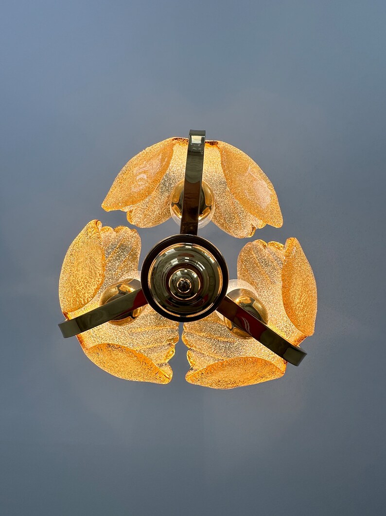 May include: A gold-toned chandelier with four frosted glass shades. The shades are shaped like petals and have a textured surface.