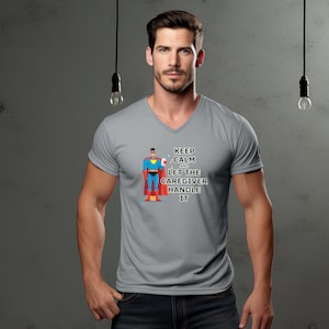 Könnte beinhalten: Graues V-Ausschnitt-T-Shirt mit einem Comic-Superhelden, der ein Erste-Hilfe-Set hält. Der Text auf dem Shirt lautet "Keep Calm and Let the Caregiver Handle It."