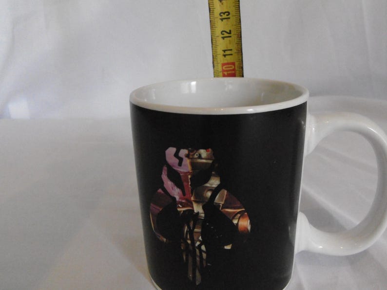 May include: A black ceramic mug with a white interior and handle. The mug features a colorful graphic of a character from a science fiction franchise. The mug is approximately 4 inches tall.