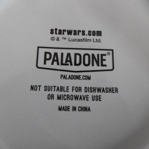 May include: White ceramic item with black text that reads "starwars.com", "PALADONE", and "PALADONE.COM". The text "NOT SUITABLE FOR DISHWASHER OR MICROWAVE USE" is also visible. The item is made in China.