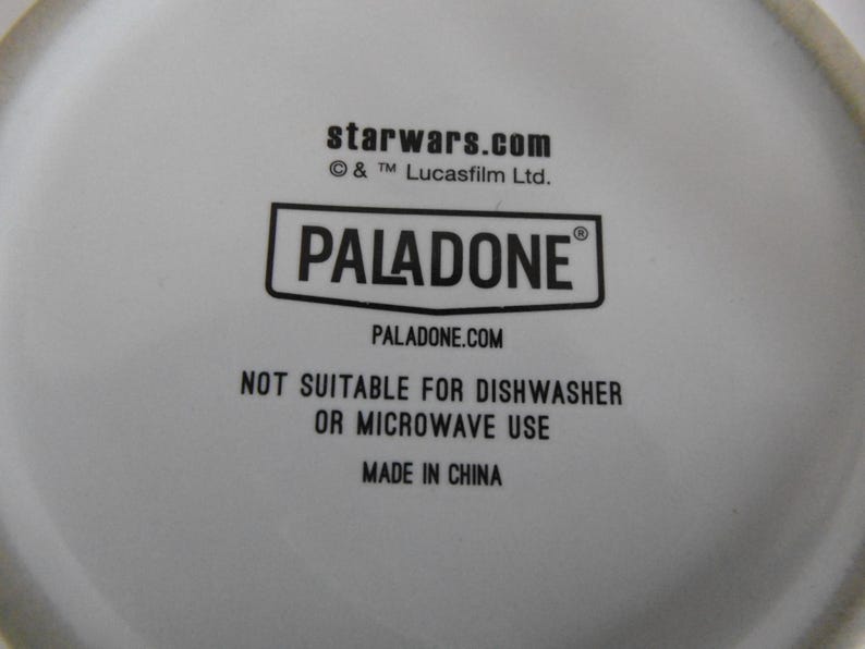 May include: White ceramic item with black text that reads "starwars.com", "PALADONE", and "PALADONE.COM". The text "NOT SUITABLE FOR DISHWASHER OR MICROWAVE USE" is also visible. The item is made in China.